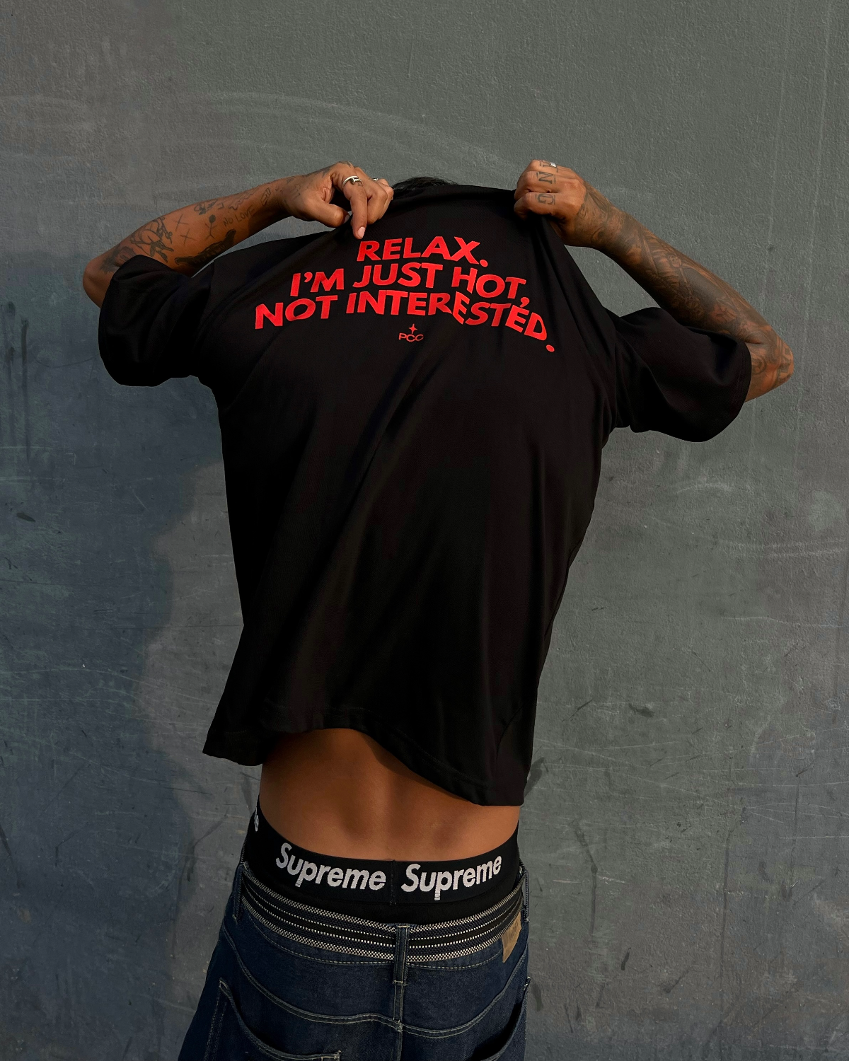 Persona usando polo negro oversize de Peruvian Cool Club con estampado rojo en la espalda: “Relax, I’m Just Hot, Not Interested”.