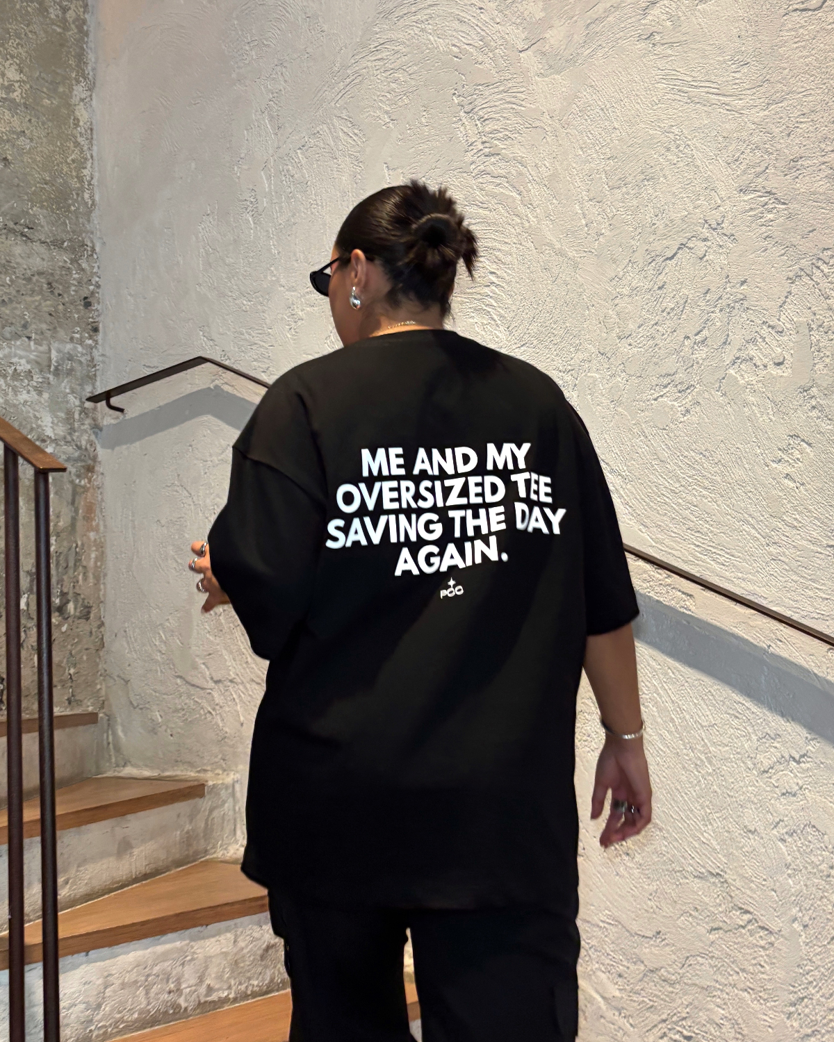 Mujer usando polo negro oversize de Peruvian Cool Club con estampado blanco en la espalda: “Me and My Oversized Tee Saving the Day Again”.